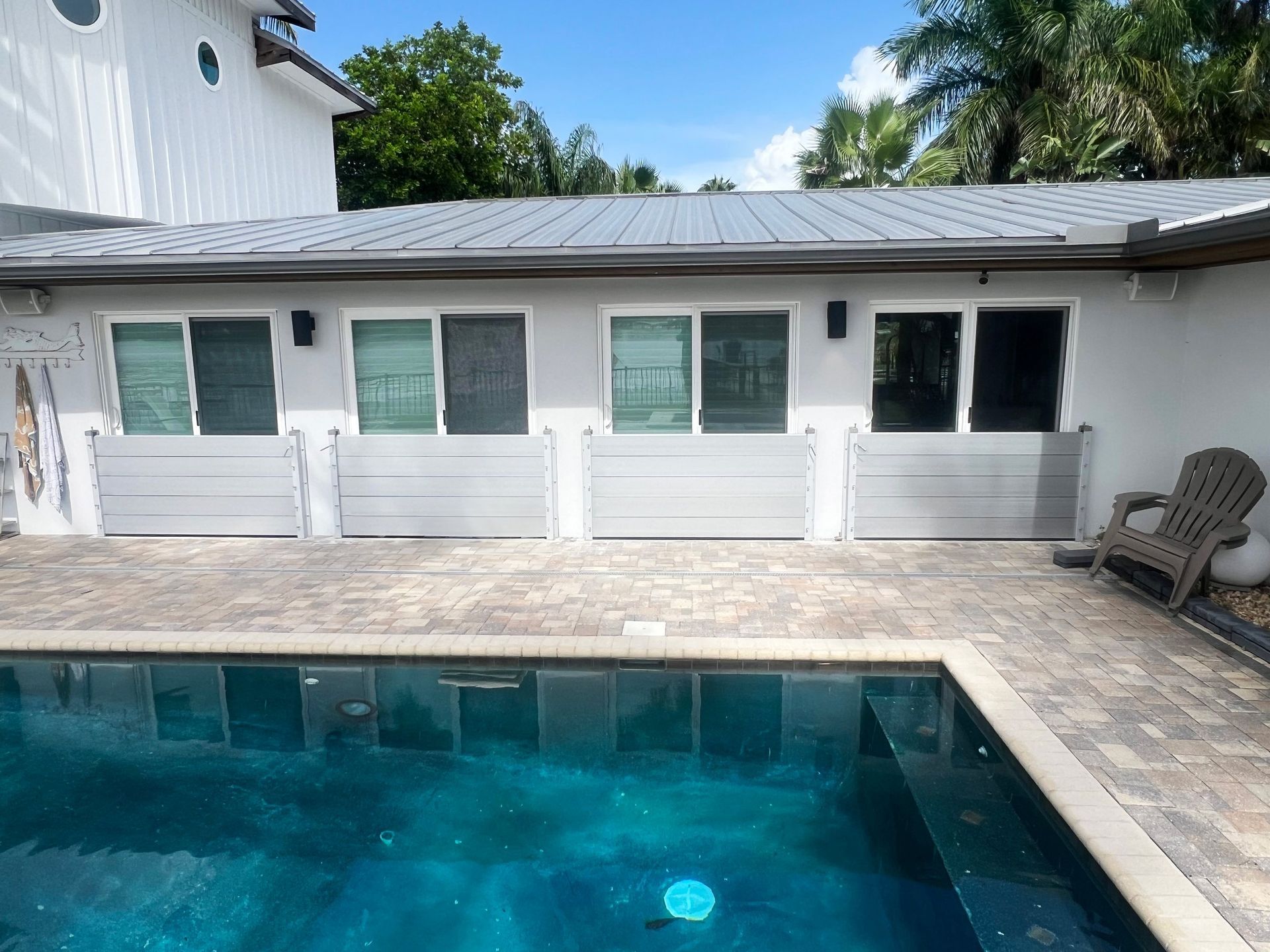 Poolside view with aluminum flood barriers installed below windows on a building with a gray metal roof.