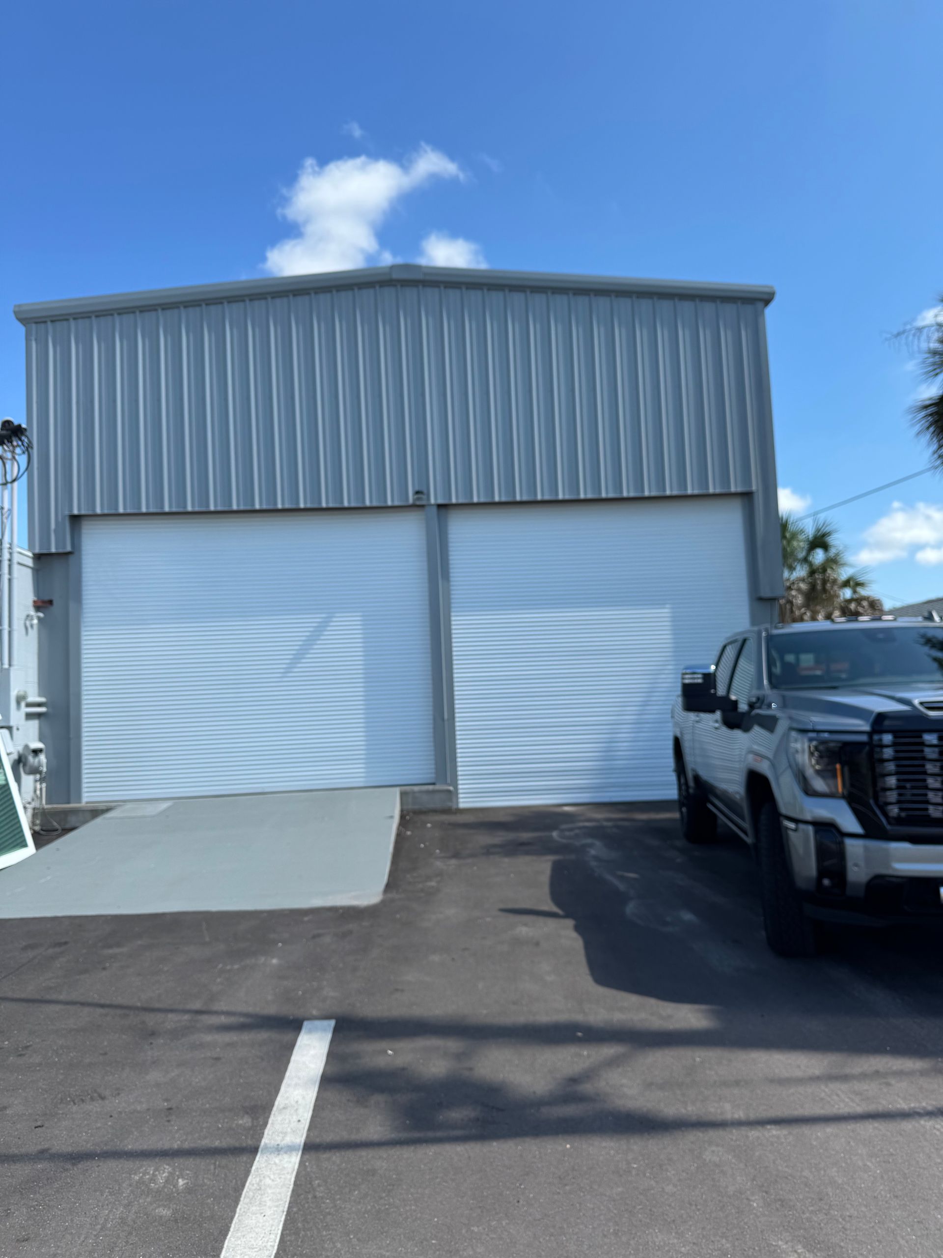 Metal building with white doors, ramp, and parked truck on a sunny day.
