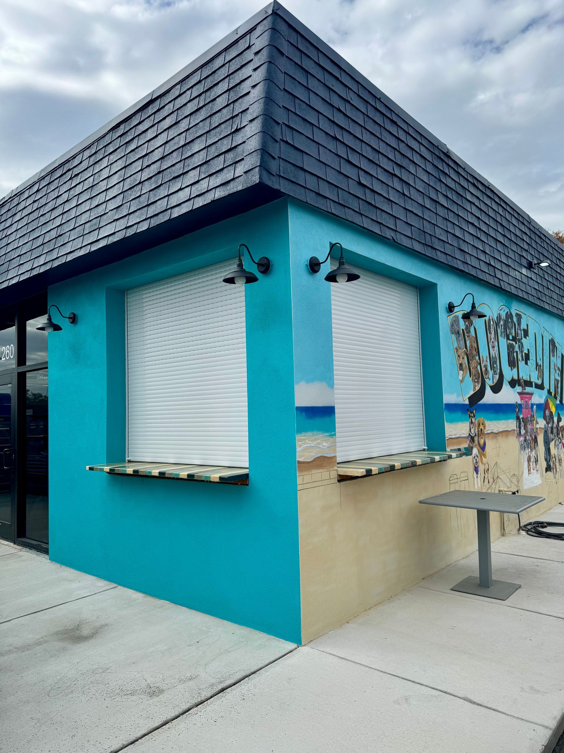 Turquoise food kiosk with white shutters, black roof, and a mural.