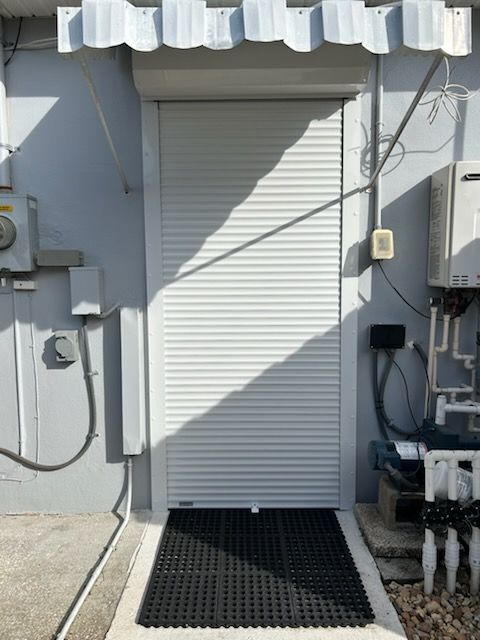 Exterior view of a building with a white roll-up door, black mat, and gray walls.