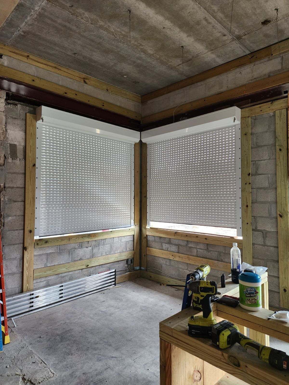 Interior room with two white, perforated security shutters installed; unfinished walls and wooden framing.