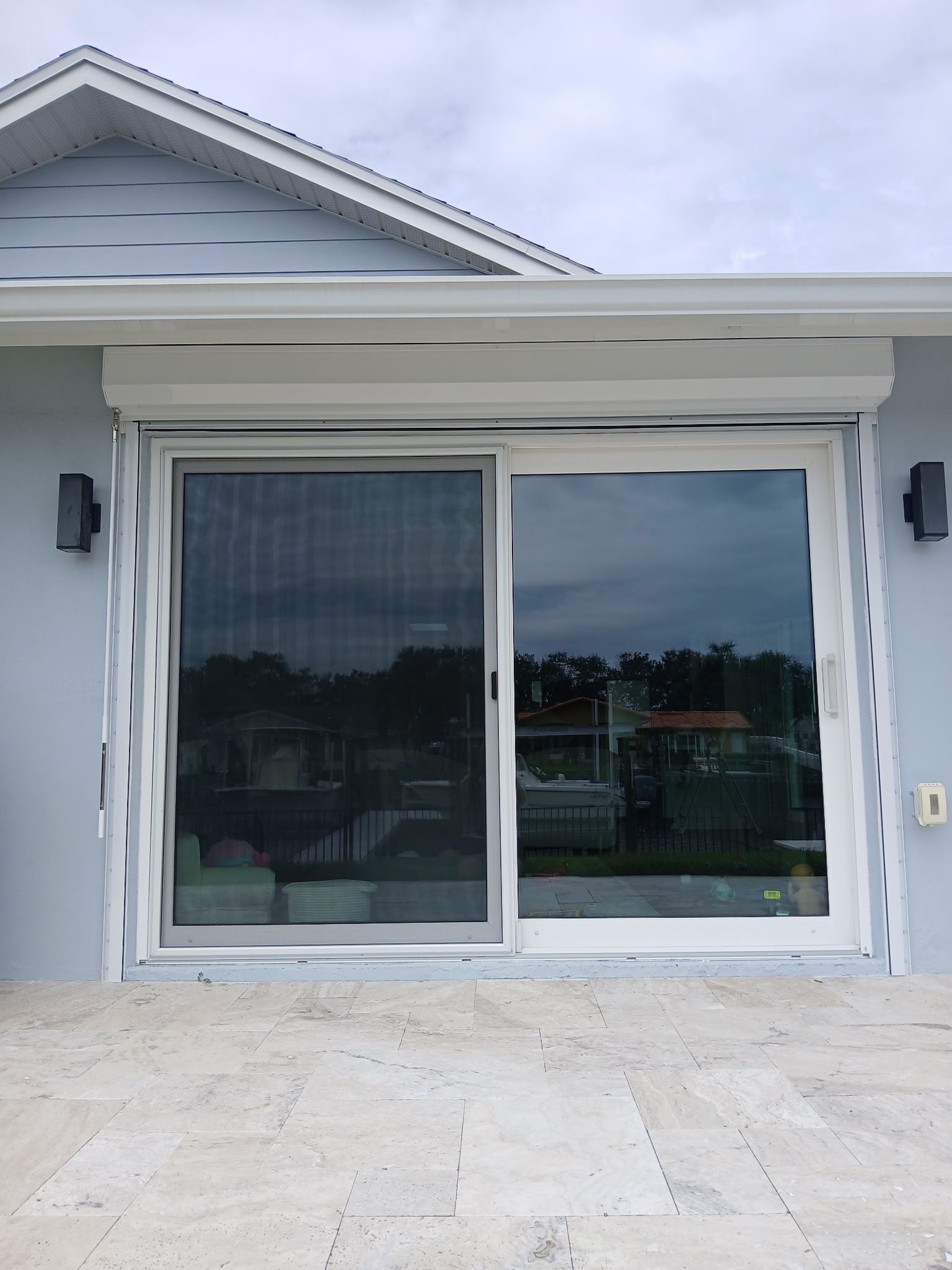 Sliding glass door with hurricane shutters, light blue exterior, white trim. Overcast day.