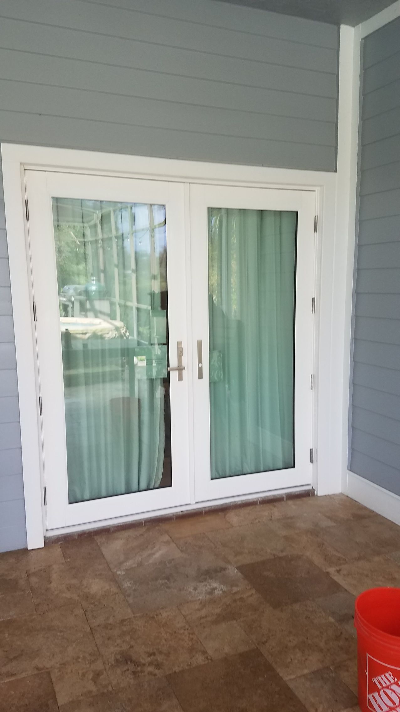 White double doors with glass panels and sheer curtains; on a porch.