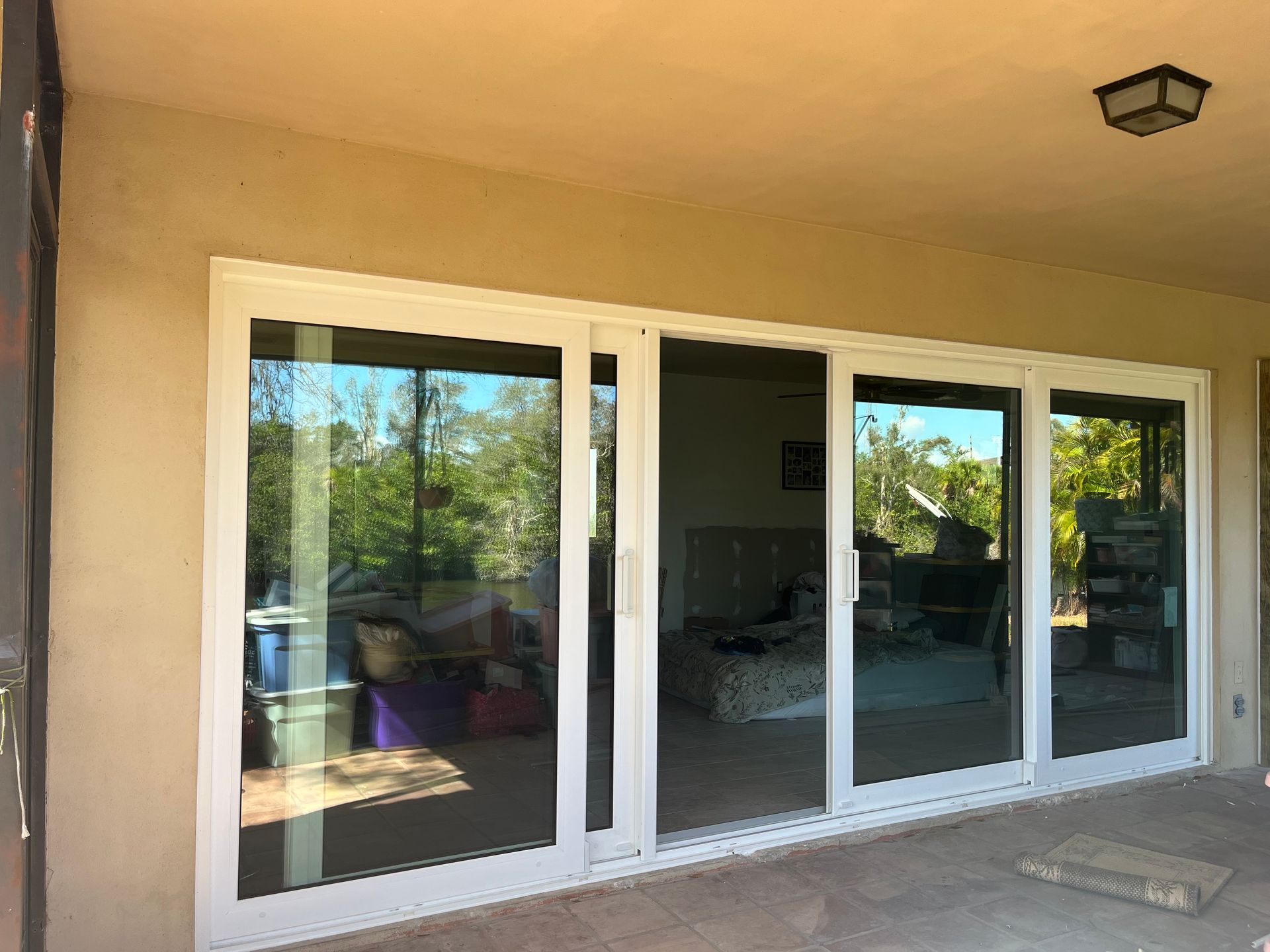 Sliding glass doors with white frames on a patio, reflecting outdoor trees and a room's interior.