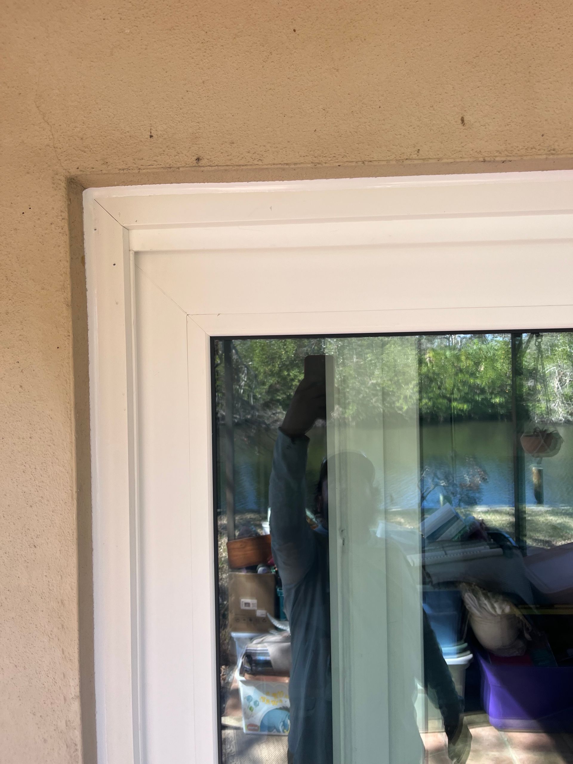 White-framed window against a beige stucco wall, reflecting trees and a person.