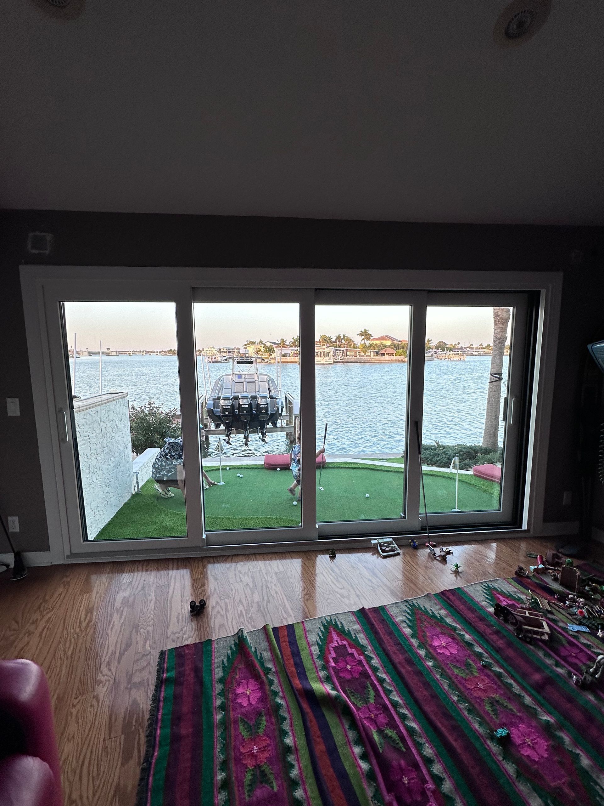 Sliding glass doors overlooking a waterfront with a boat dock and water. Interior with a rug and wooden floor.