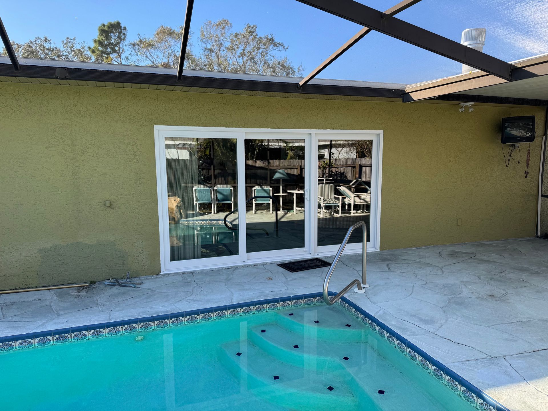Swimming pool next to a patio door. Blue water, white door frame, and green stucco wall.