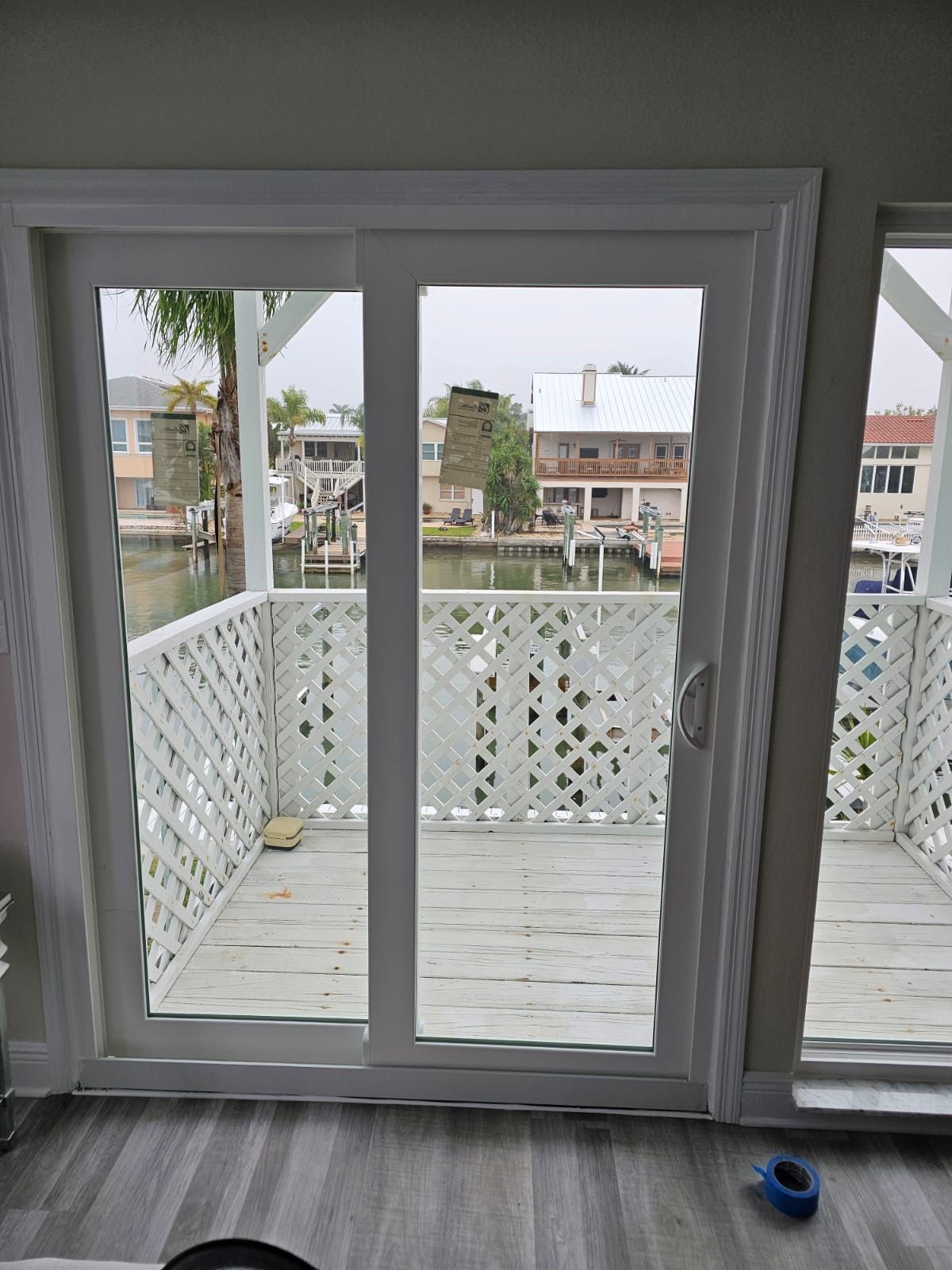 Sliding glass door opening to a white latticework balcony overlooking a canal with houses.