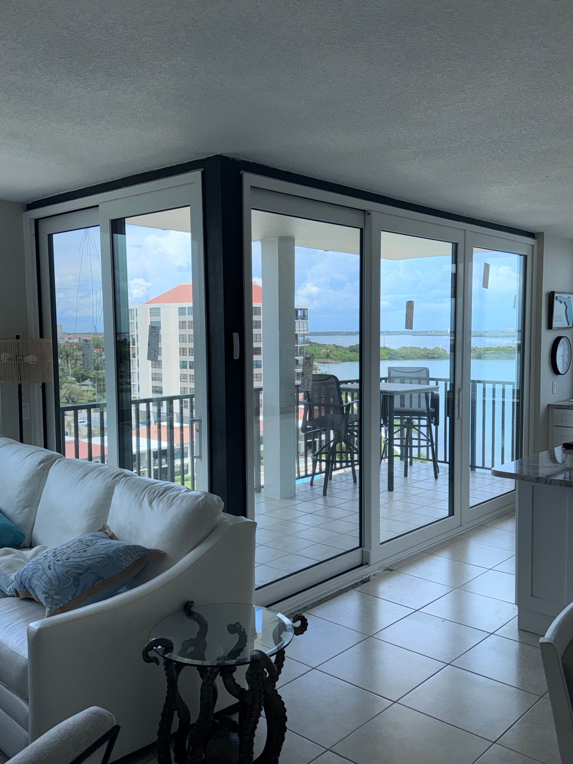 Bright condo interior with white couch, glass doors to balcony, water view.