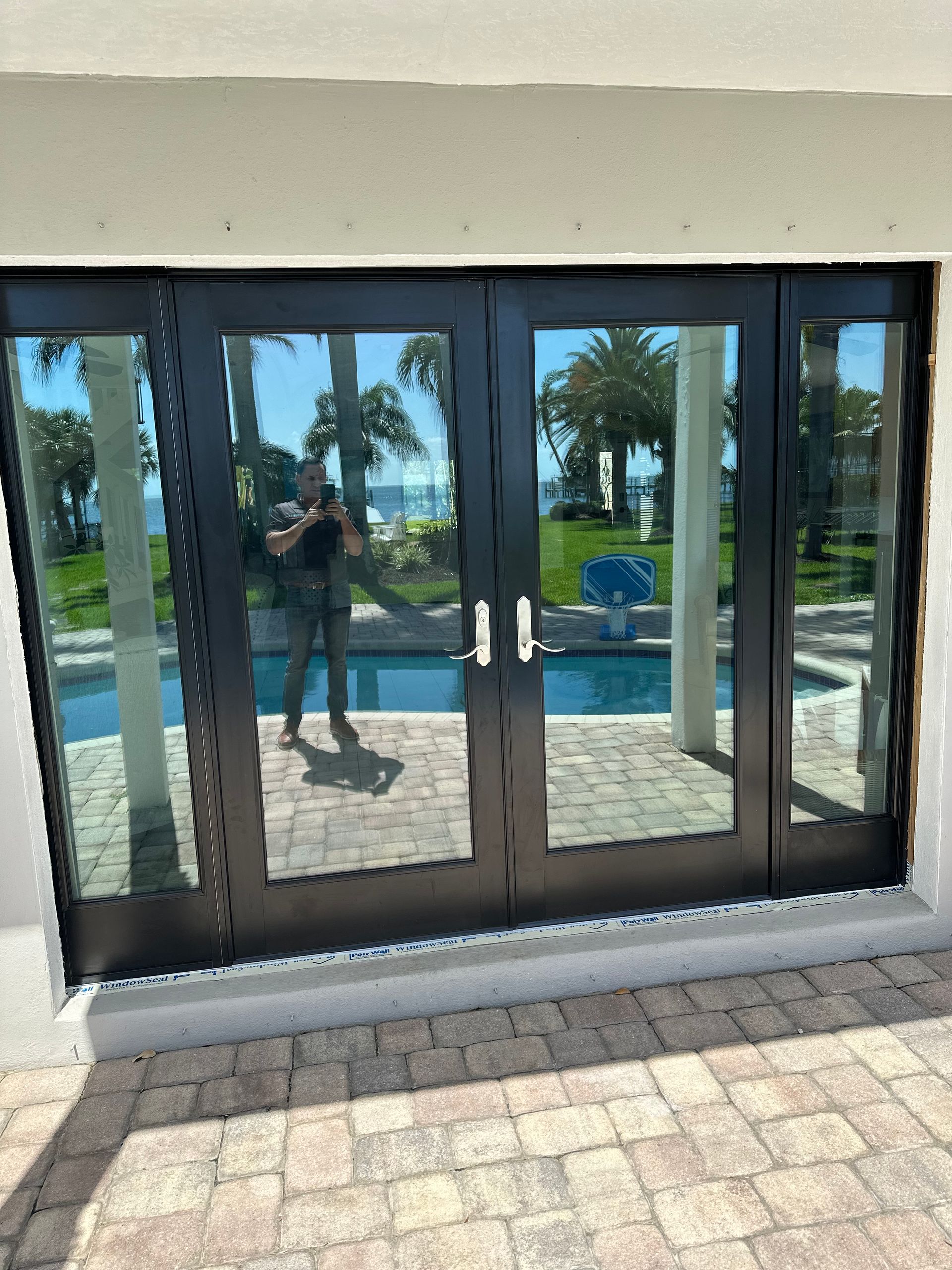 Black glass doors overlooking a pool and ocean view; person reflected.