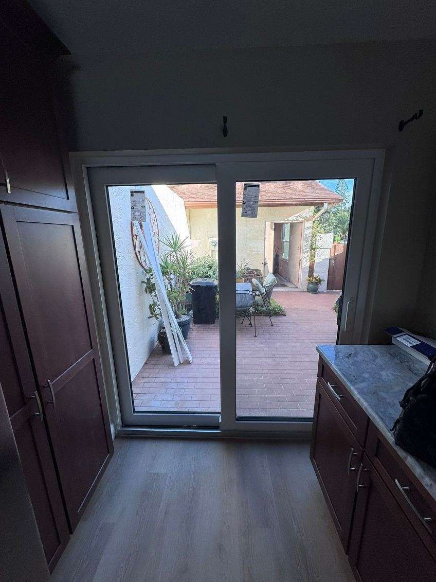 Sliding glass door opens to a backyard with wooden deck, ladder, plants, and a building.