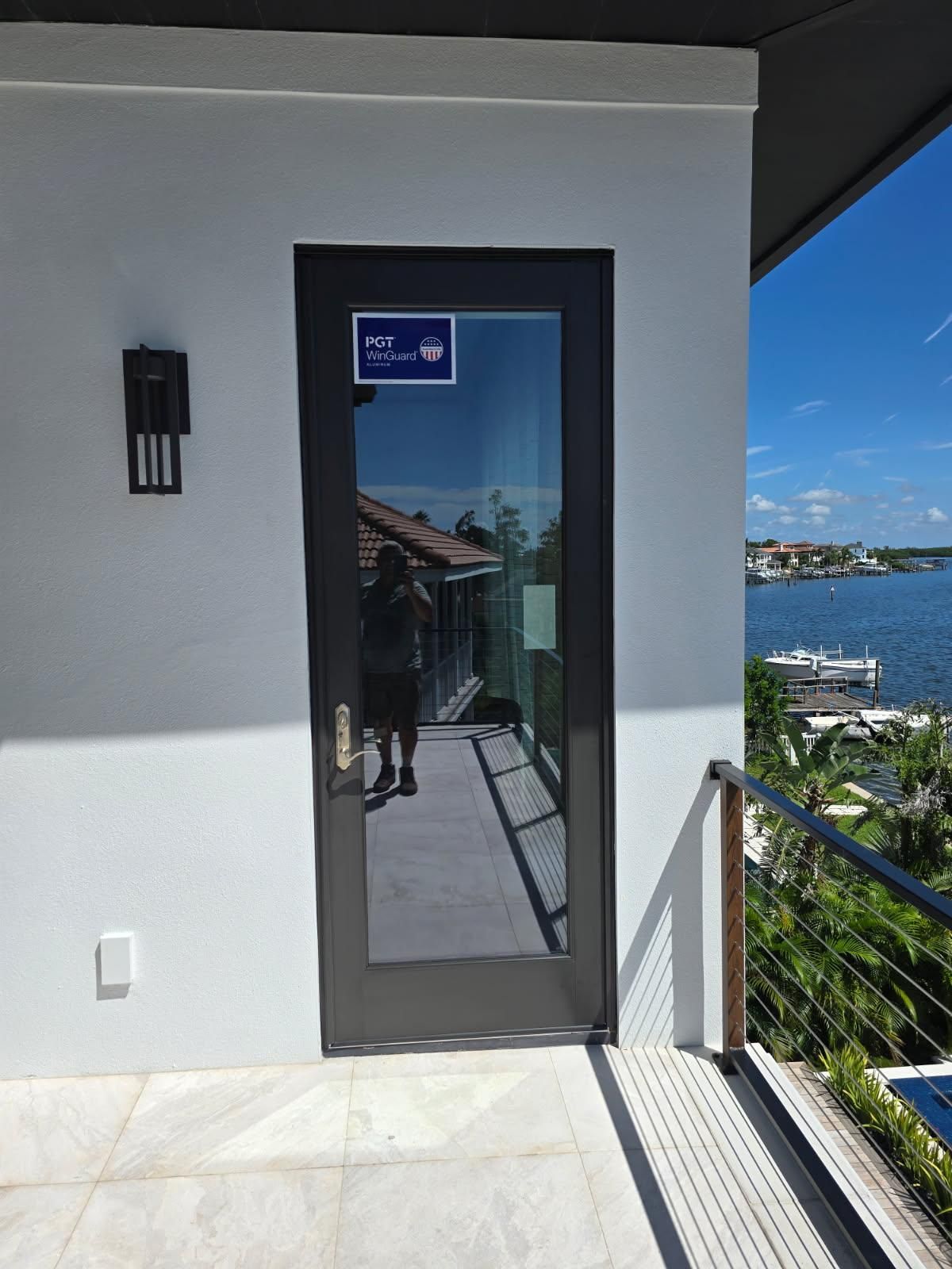 Glass door on a balcony with a view of water and a person reflected in the glass.