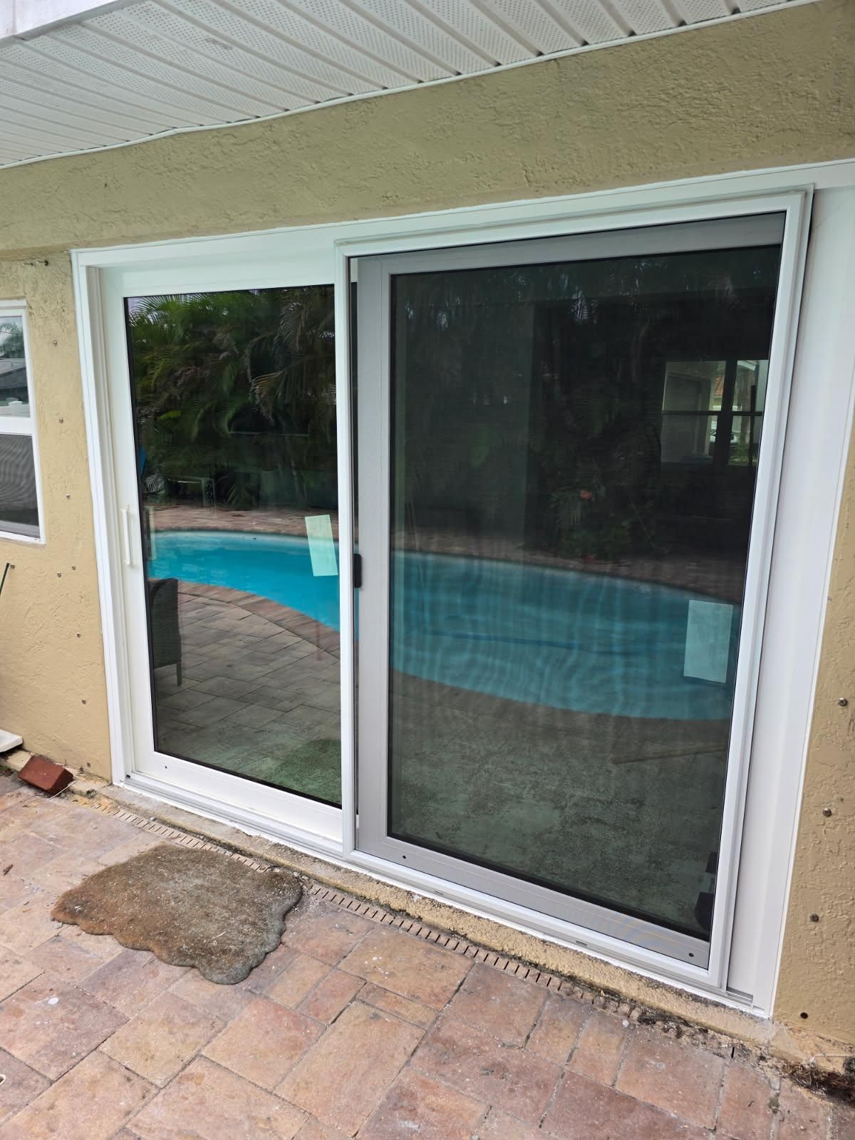 Sliding glass door, one side open, overlooking a pool. Tan stucco wall and brick patio.