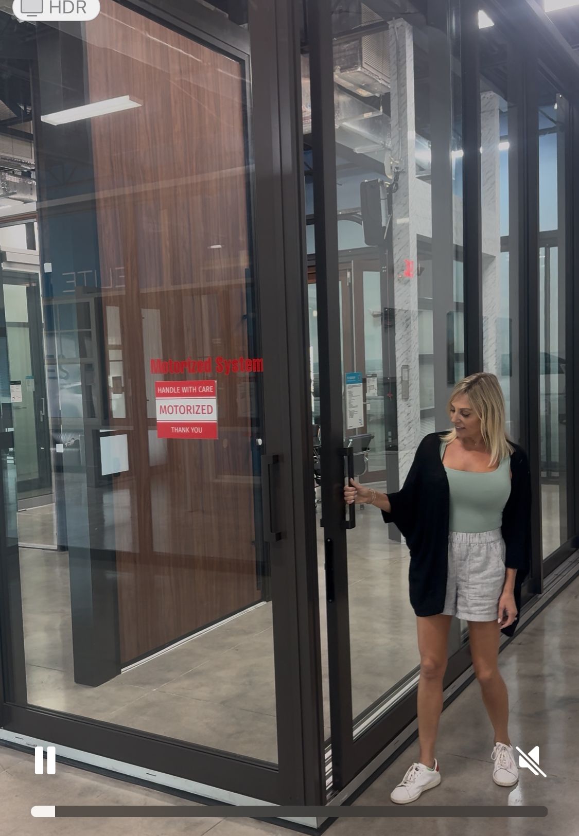 Woman opening large glass door, indoor showroom. The door has dark frame, and a wood panel.