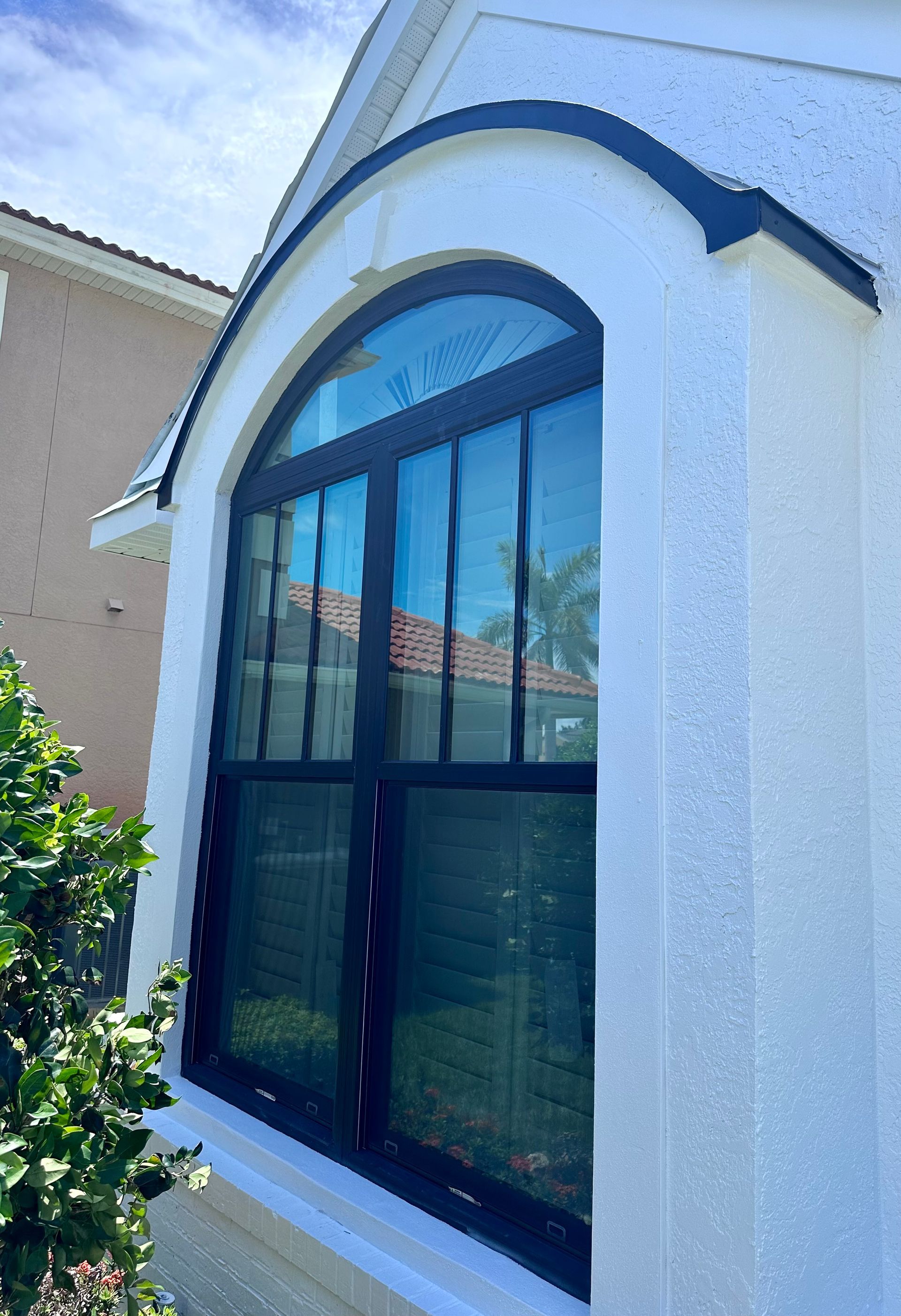 Black-framed arched window on white stucco house, framed by trim, with blue sky in background.