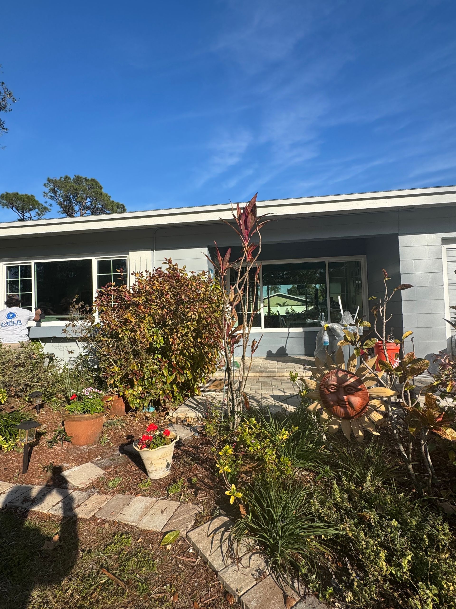 House exterior with a garden in front. Gray siding, windows, pots, plants. Bright blue sky.