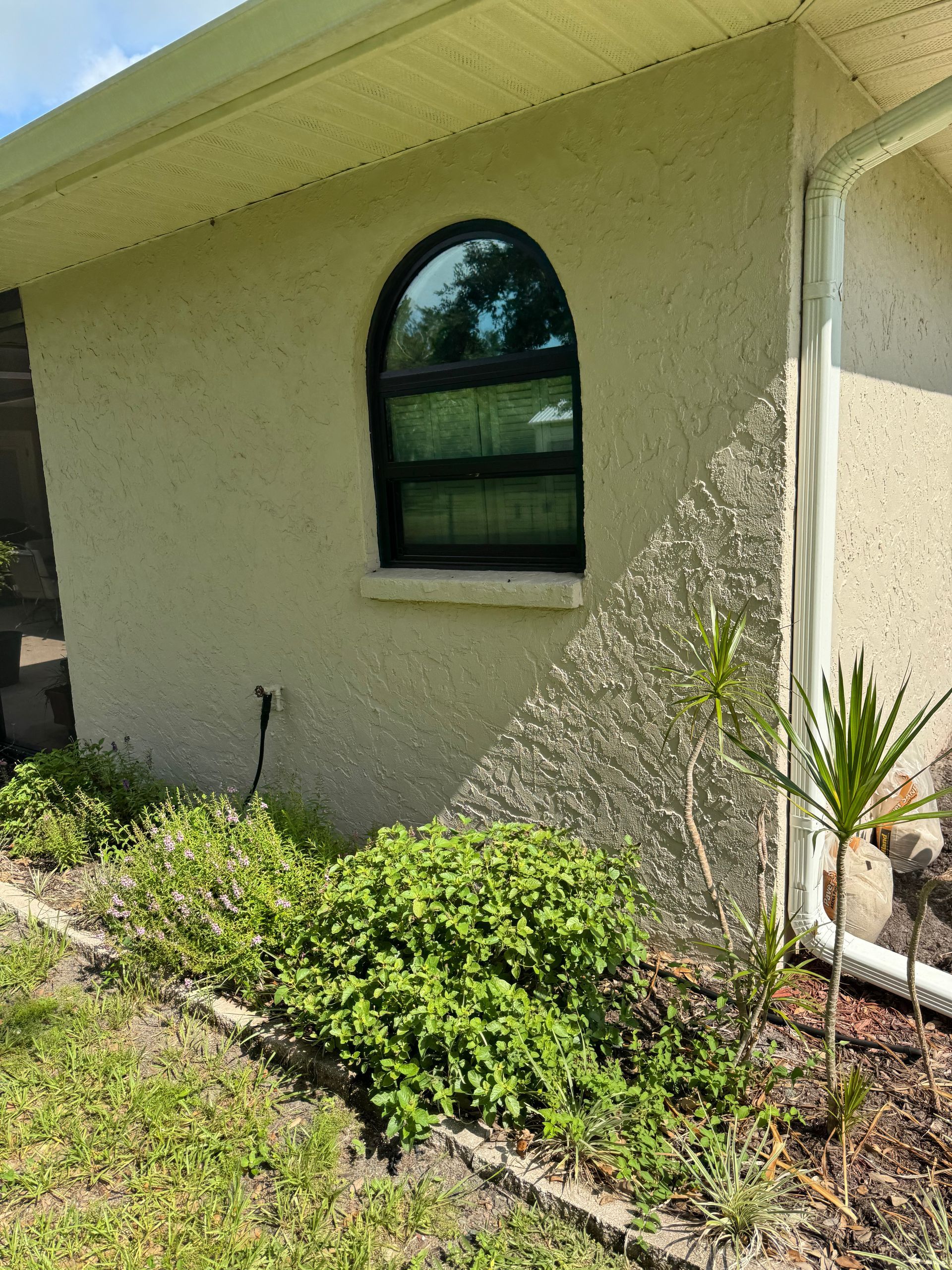 Tan stucco building with arched window and landscaping.