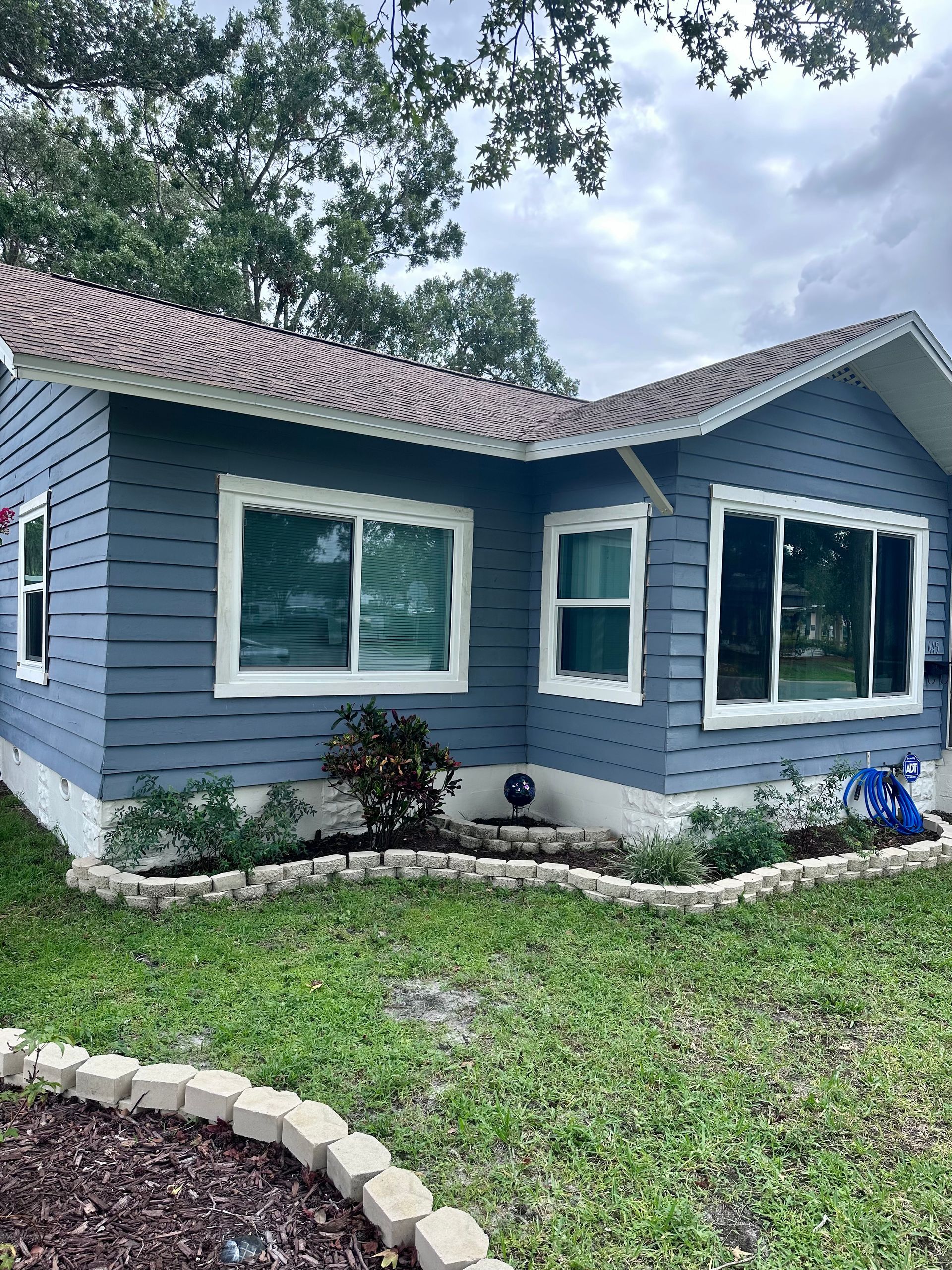 Blue house with white trim, brown roof, and small front yard with a garden bed.