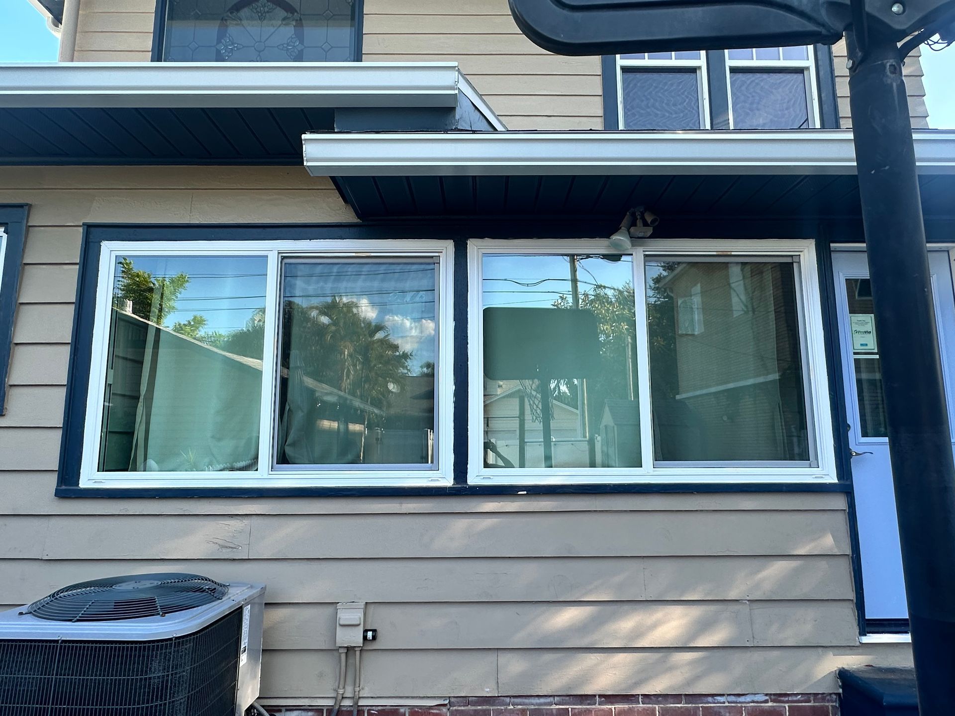 Tan house with white-framed windows, dark trim, and a cooling unit.