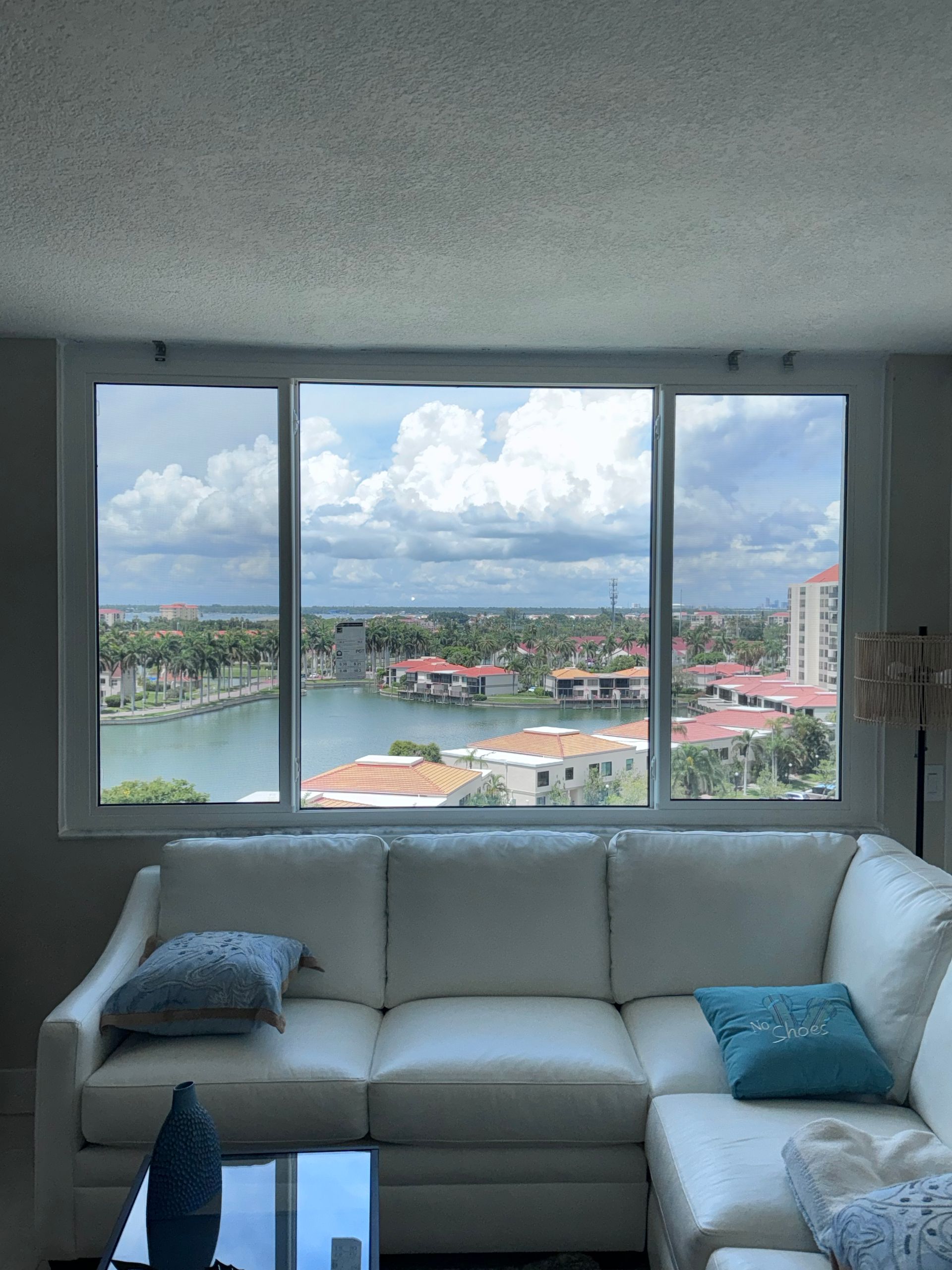 White sectional sofa in front of large window overlooking a waterway and buildings under a cloudy sky.