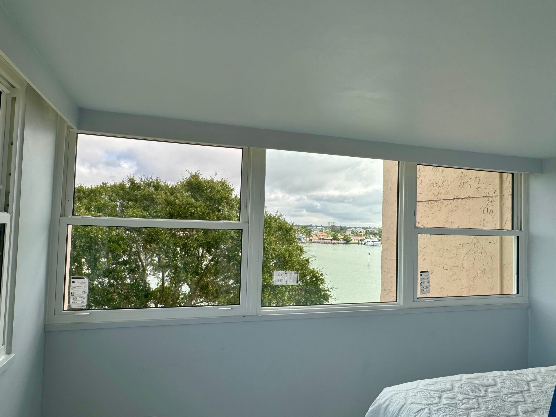 Three-pane window overlooking a body of water and trees on a cloudy day, inside a room with light blue walls.