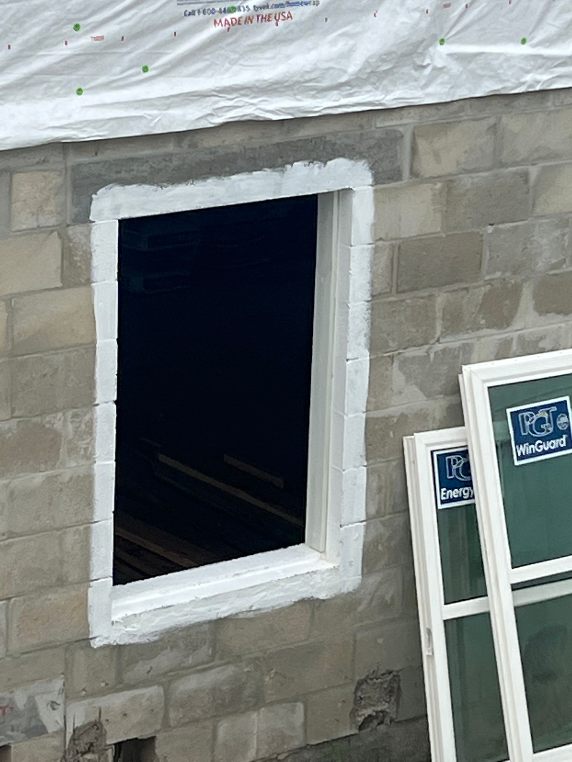 Window frame opening in a concrete block wall, caulked with white sealant. New window leaned against the wall.