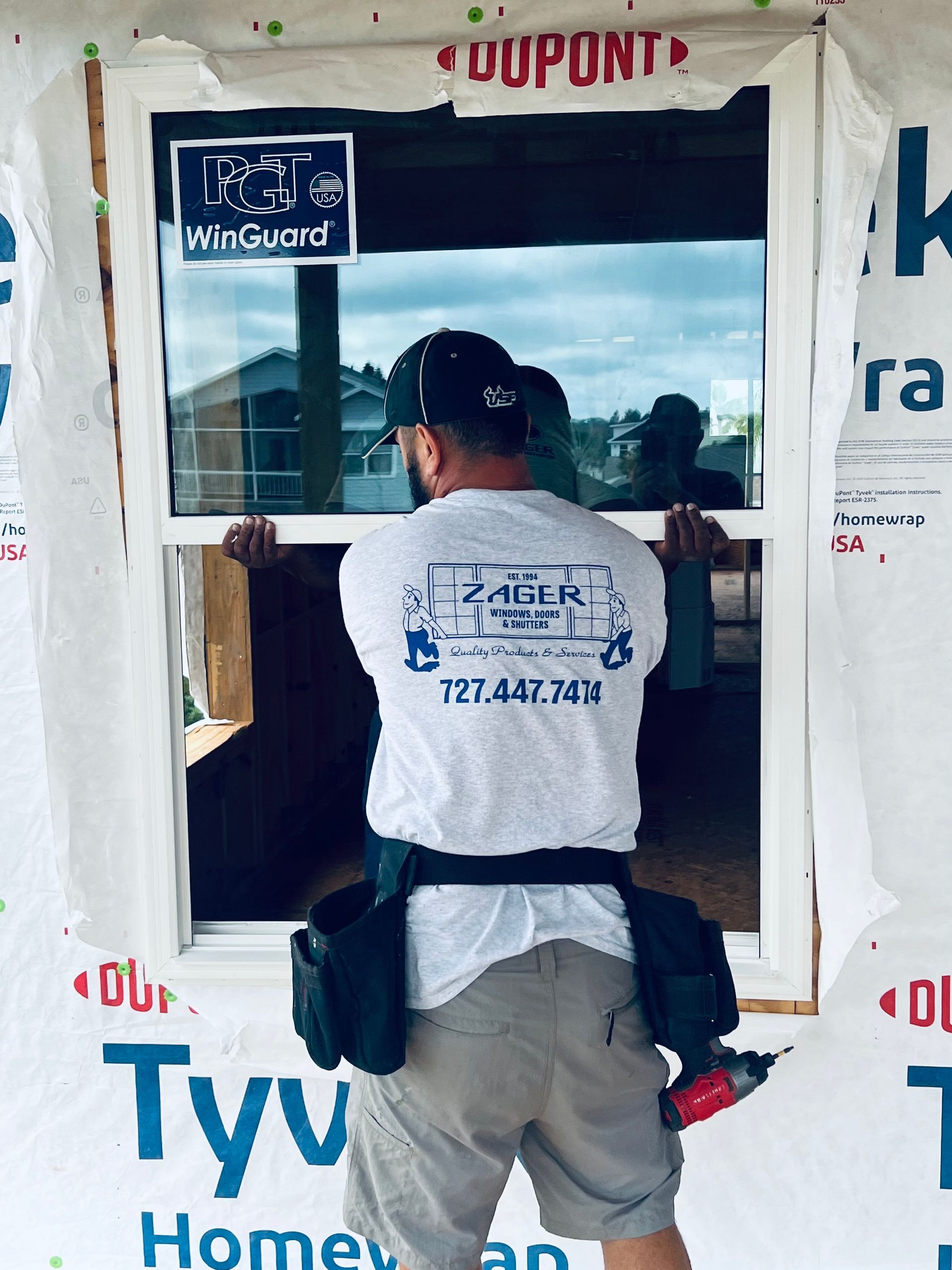 Man installing window, wearing white shirt and tool belt. Exterior shot, house under construction.