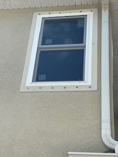 Window set in beige stucco wall with white trim and a white gutter.