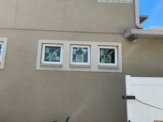 Three square windows in light-colored frame on a tan stucco wall. White fence on the right.