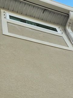 Exterior wall with a rectangular window and white trim. Beige stucco and white soffit.