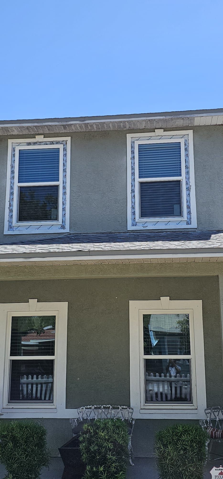 Two-story house with four windows. Green walls, white trim, blue sky.