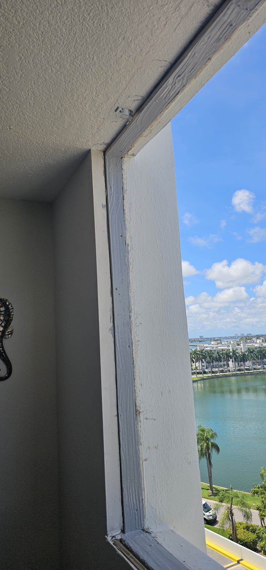 View from an open window of a white building overlooking a body of water and a city under a blue sky.