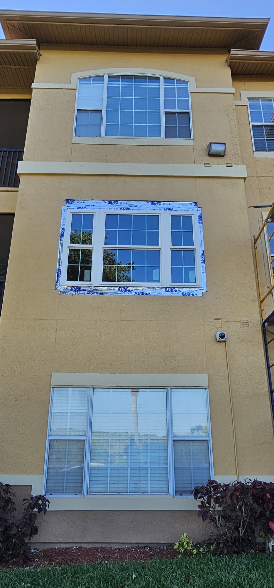 Exterior of a tan building with three windows; a blue sky is reflected in the glass.