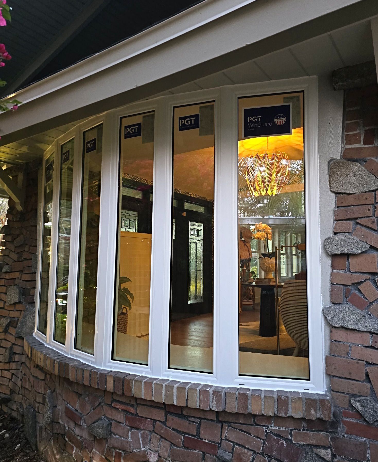 Bay window with white frames set into brick and stone wall, reflecting interior of a home.