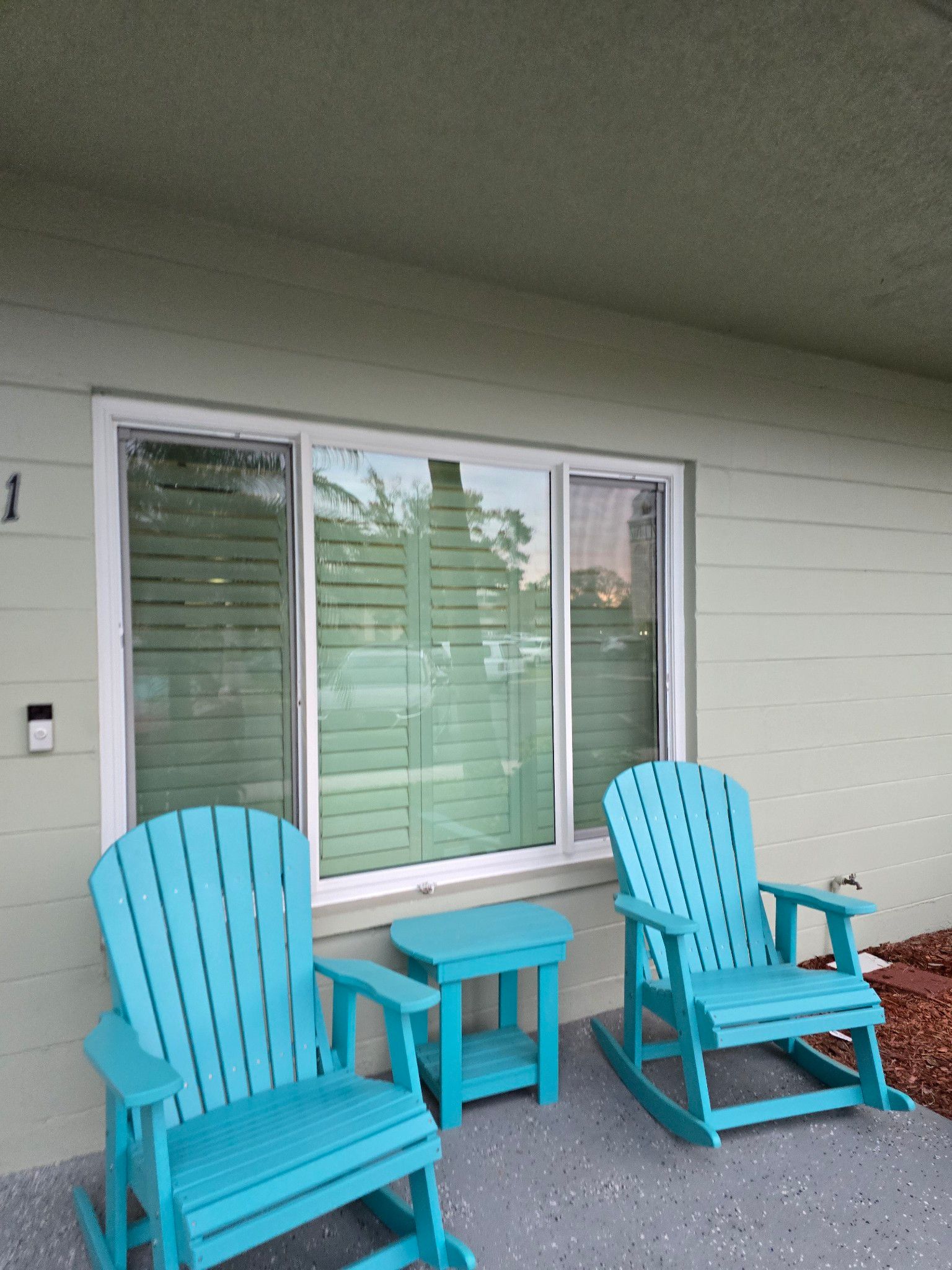 Two turquoise rocking chairs and small table on a patio, in front of a window.