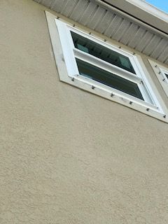 Tan stucco wall with a white-framed window. Black fastener heads are around the window frame.