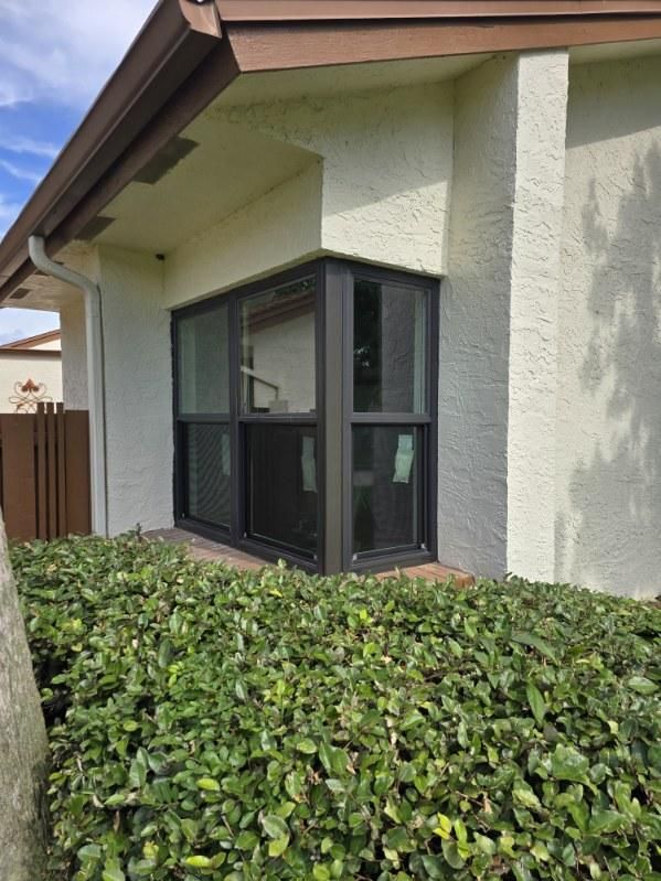 Corner window of a beige building with dark frames, behind green bushes.