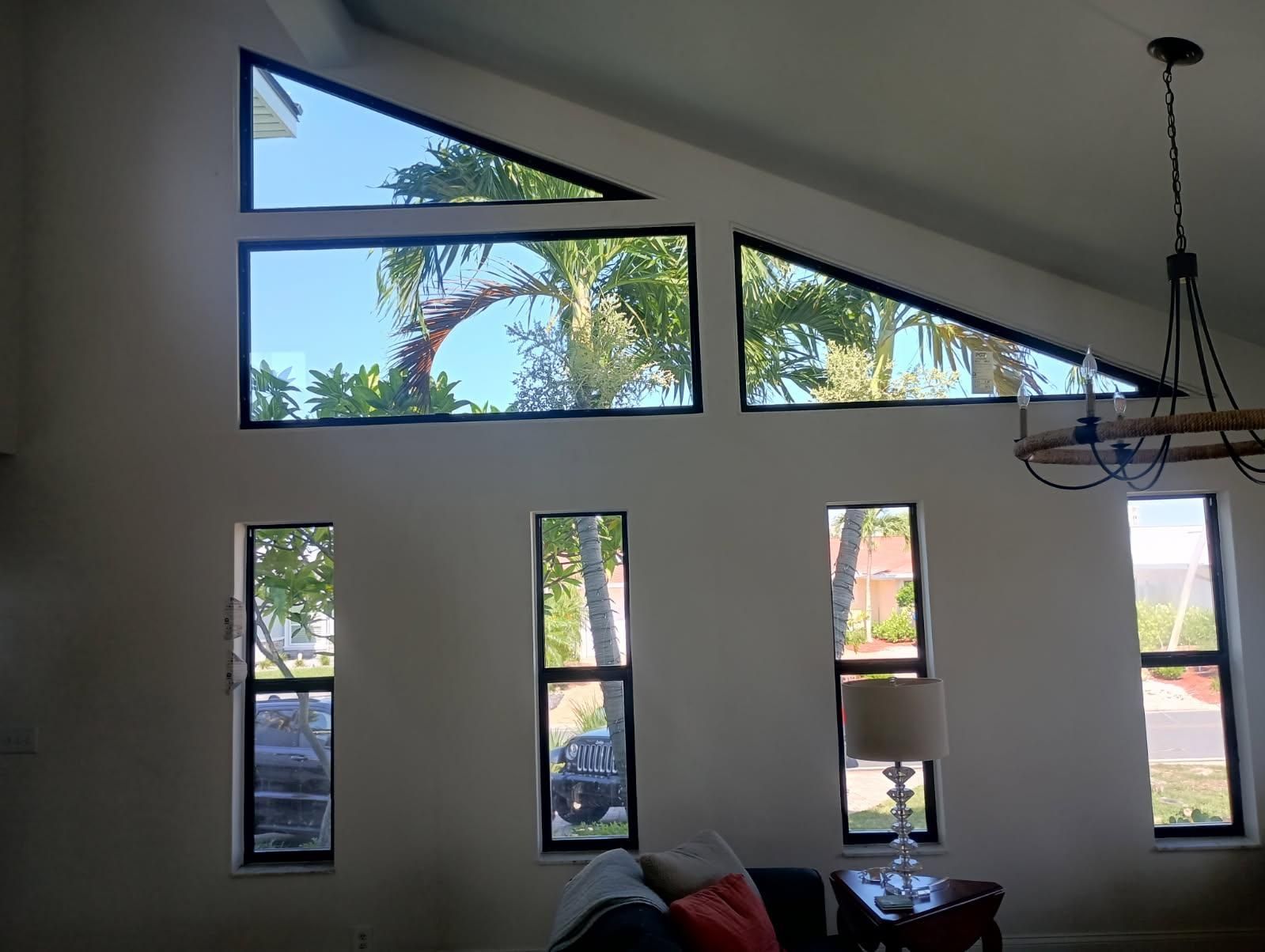 Windows with black frames in a white-walled room, showing trees and sky. A chandelier hangs from the ceiling.