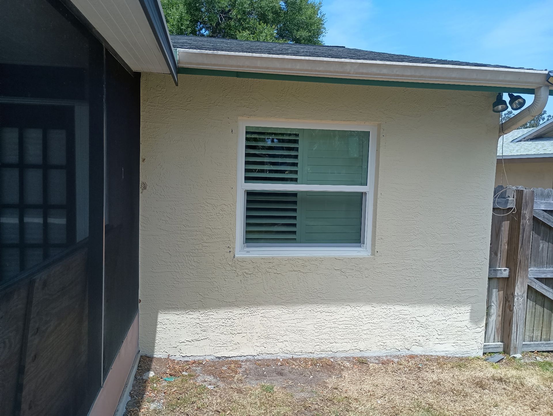 Tan stucco wall with a white-framed window. Partially visible is a screened porch and a wooden fence.