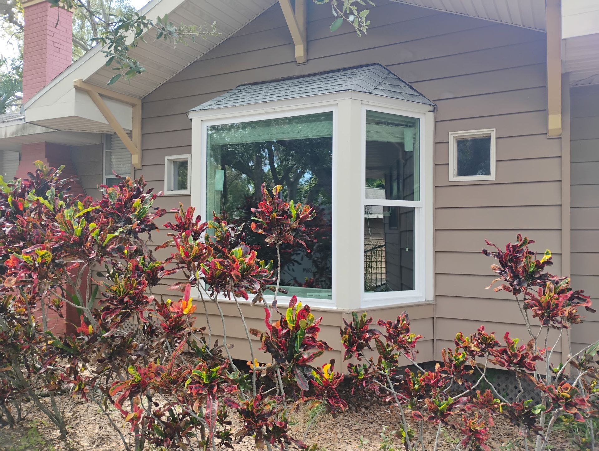 Tan house with a large bay window, surrounded by colorful bushes.