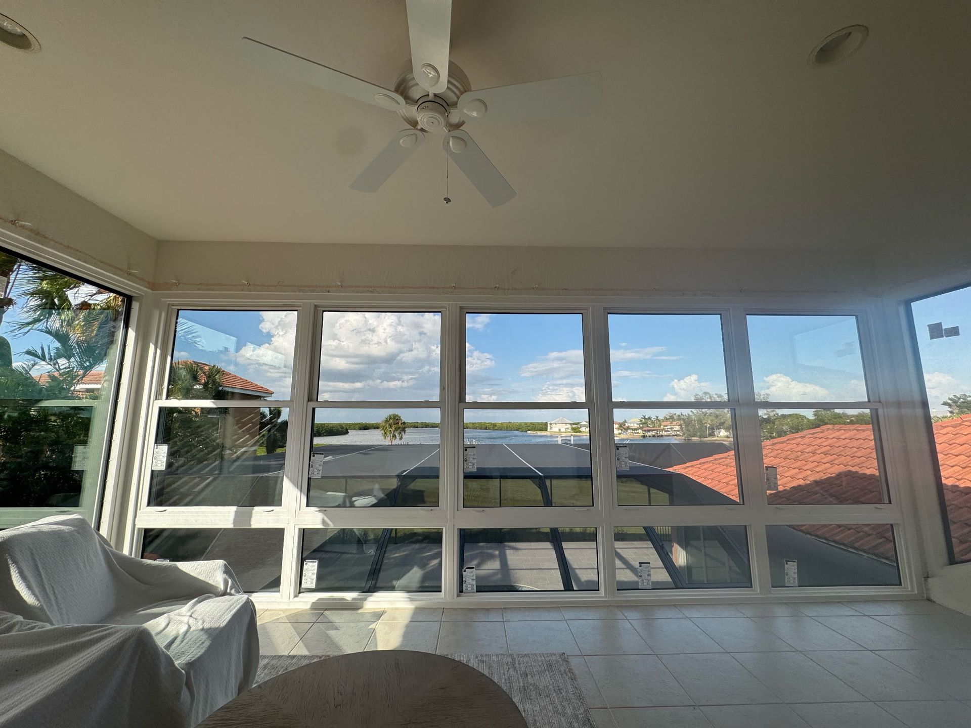 Sunroom with large windows overlooking a waterfront view, white walls, and a ceiling fan.