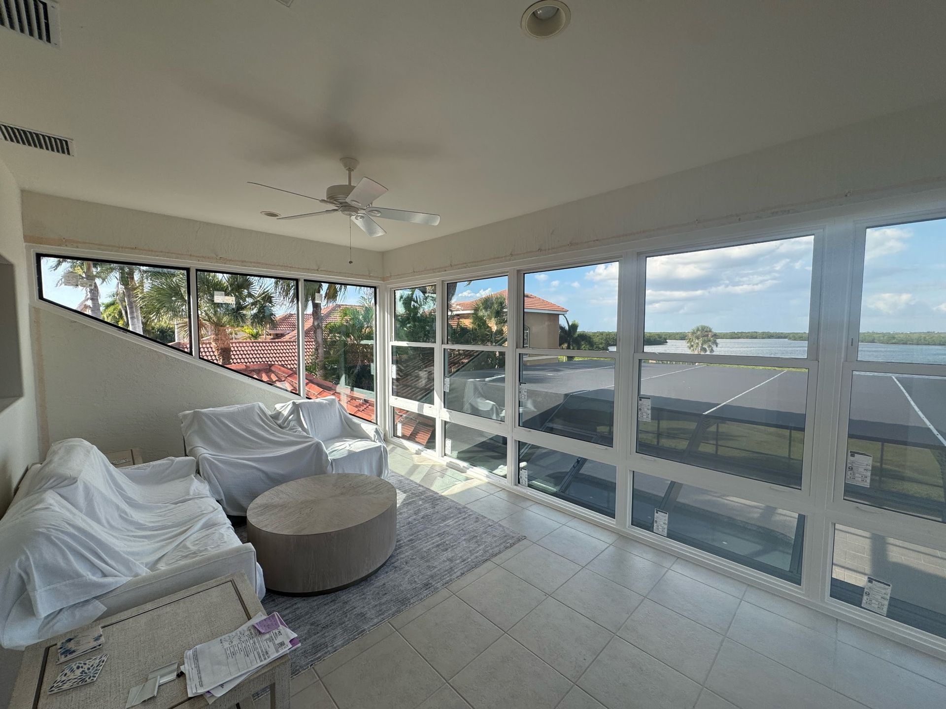 Sunroom with white walls, large windows, and a water view. Furnishings are covered in white cloth.