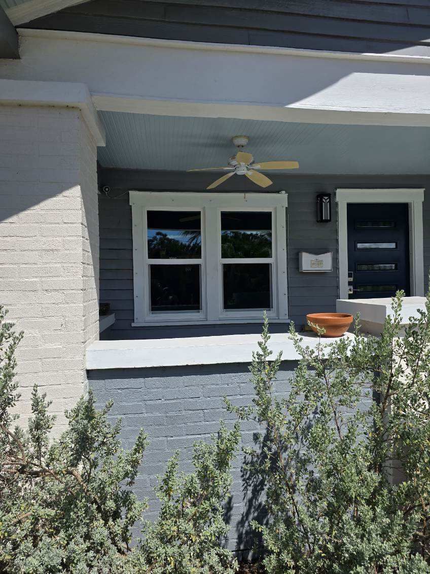 Gray and white house porch with a ceiling fan, windows, and a black door.