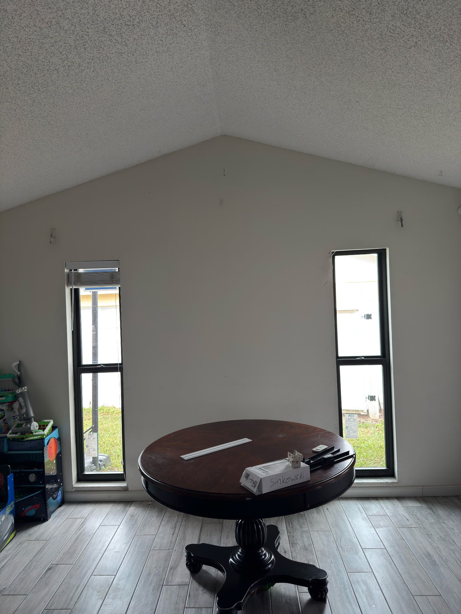 Room with a round table, two windows, and a high ceiling. Table has items on it.