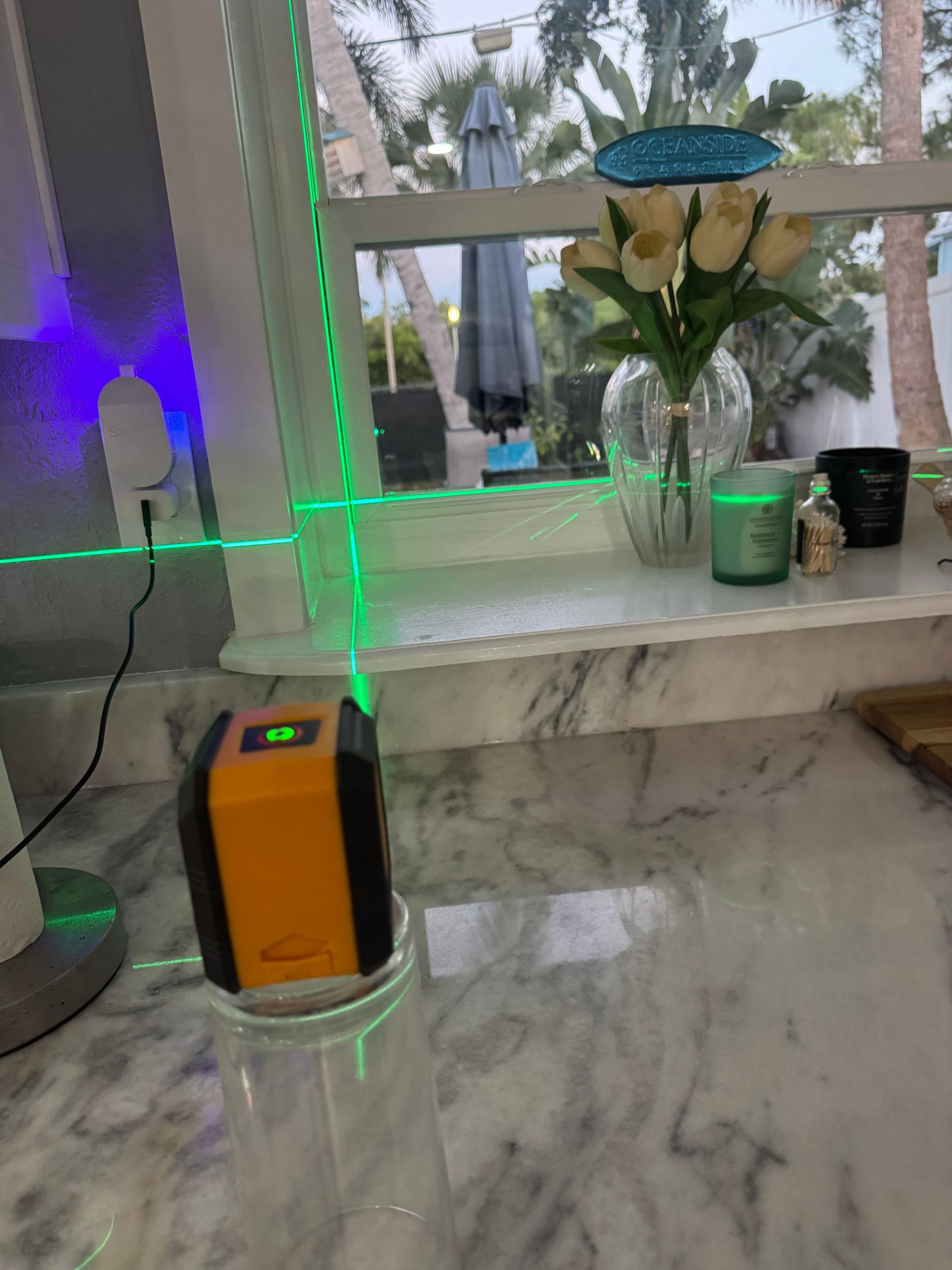 A laser level projects green lines on a marble countertop near a window.
