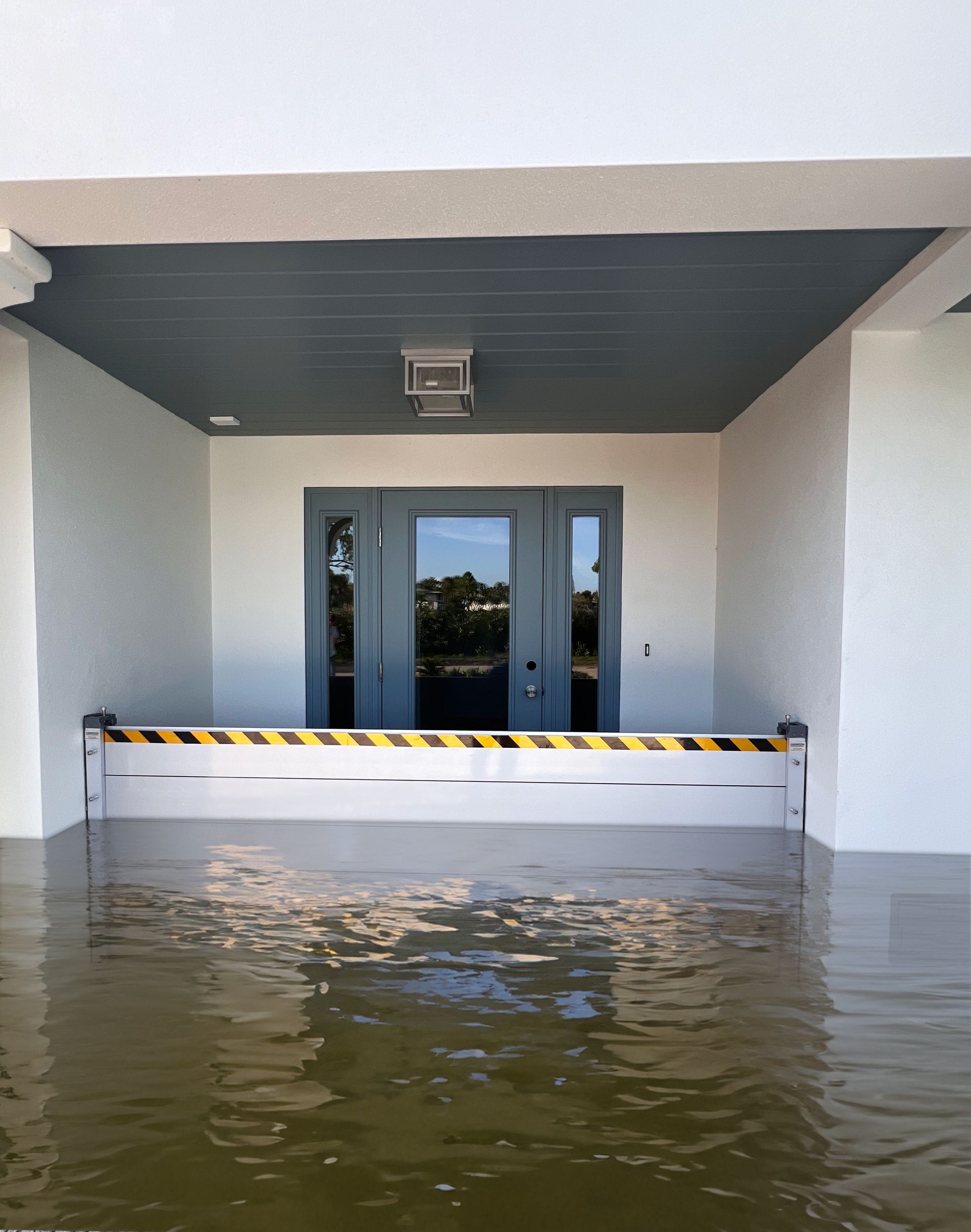 Flooding outside building entrance; flood barrier in place, water covering lower portion, blue double doors.