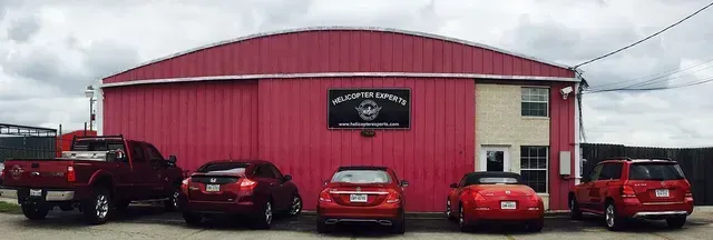 Red building with a sign and red cars parked in front under a cloudy sky.