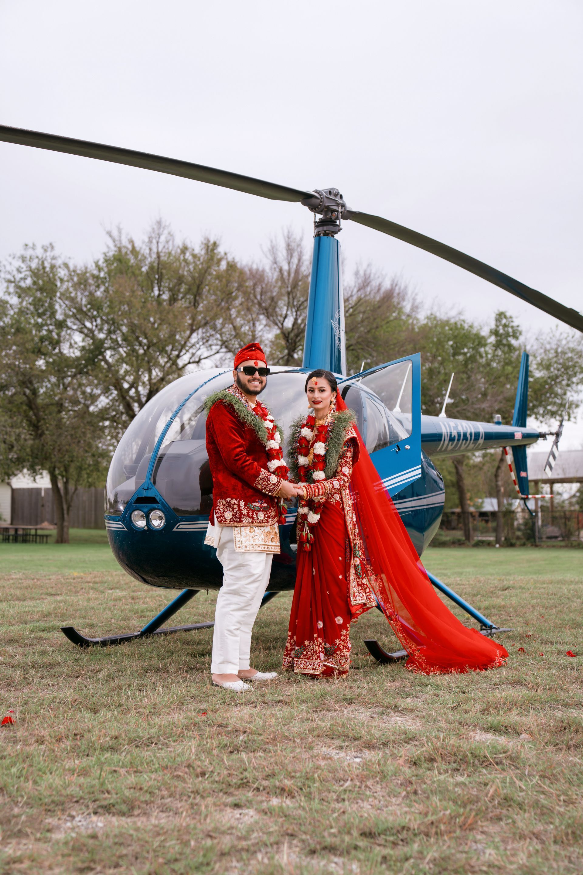 Bride and groom in front of a blue helicopter on a grassy field