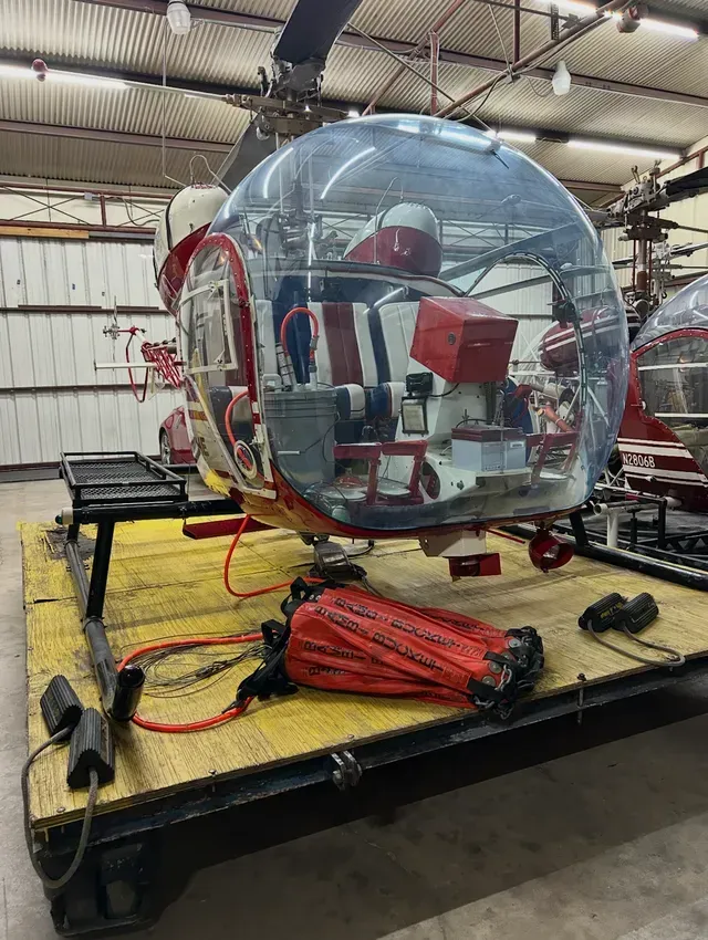 Red and white helicopter on a yellow platform inside a building, with a transparent bubble cockpit.