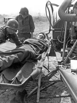 Soldier on stretcher being loaded onto a medical transport. Two other soldiers in uniform attend.